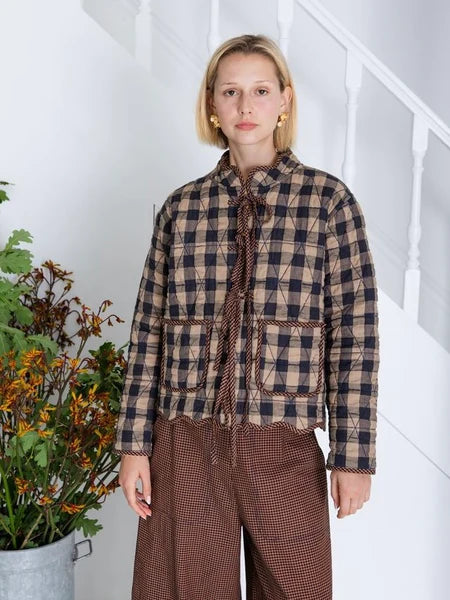 Person wearing a plaid shirt and brown pants in a minimal indoor setting