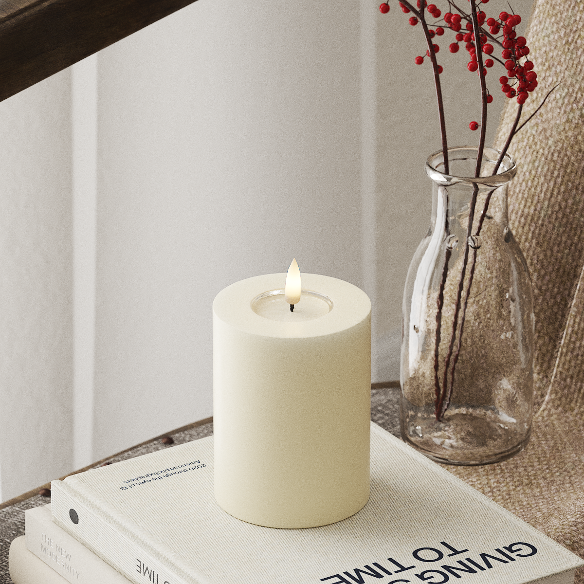 White candle on a stack of books with a vase containing red berries in the background