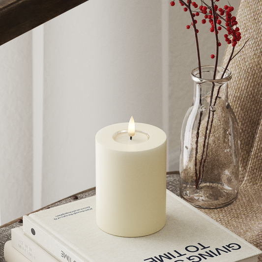 White candle on a stack of books with a vase containing red berries in the background