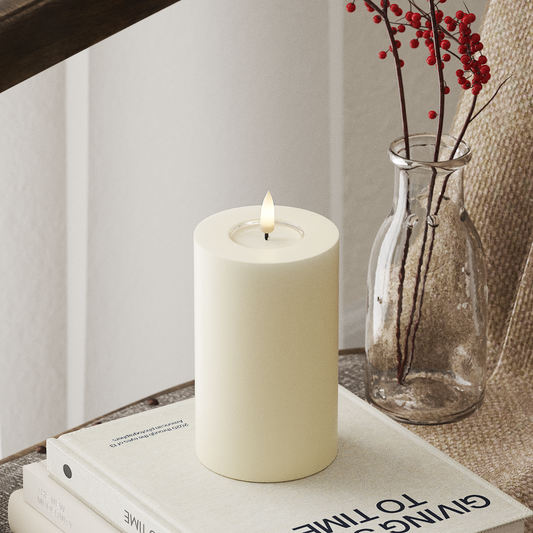White candle on a stack of books with a vase of red berries in the background