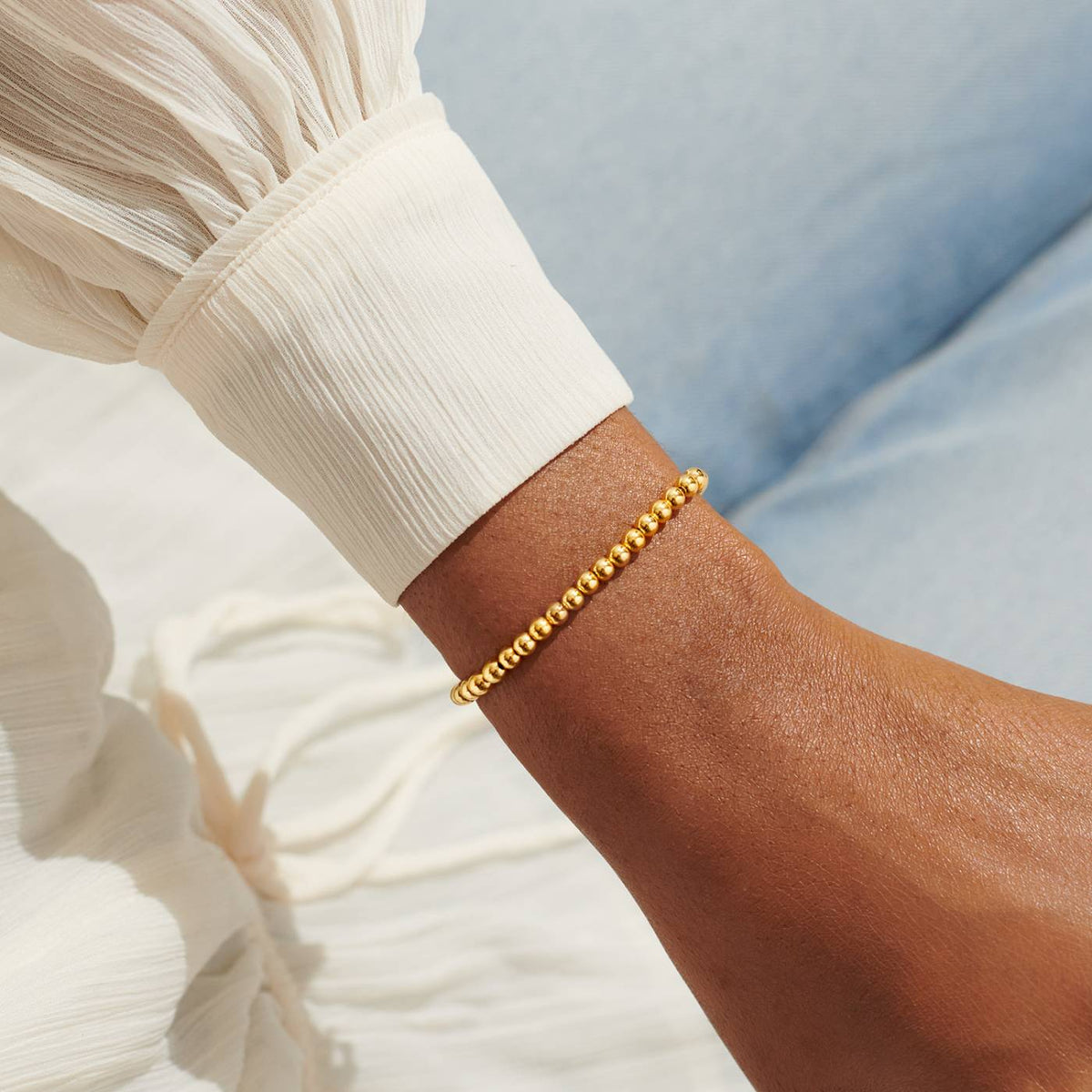 Joma Jewellery 4mm Gold Plated Stacking Bracelet - Gold bracelet on a wrist with a blurred background