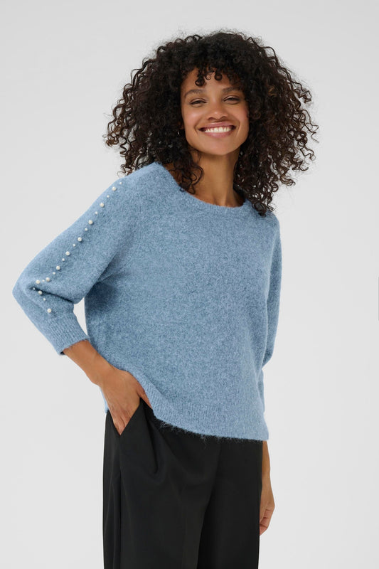 KAFFE Betty Pullover in Windward Blue. Woman wearing a blue sweater with pearl embellishments on a white background