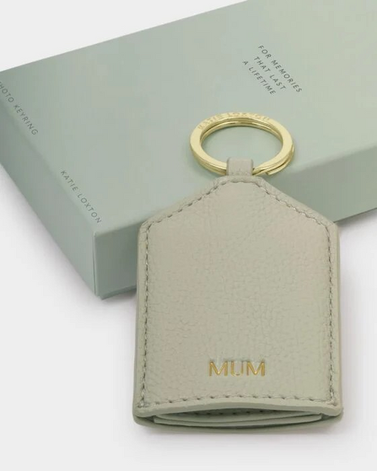 Light gray leather key fob with gold ring and 'MUM' engraving on a light green box background.