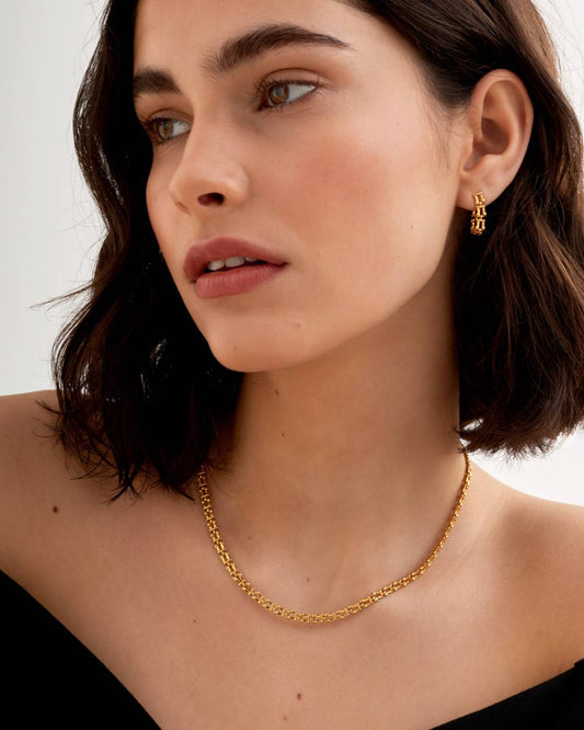 Woman wearing a gold necklace and earrings against a neutral background