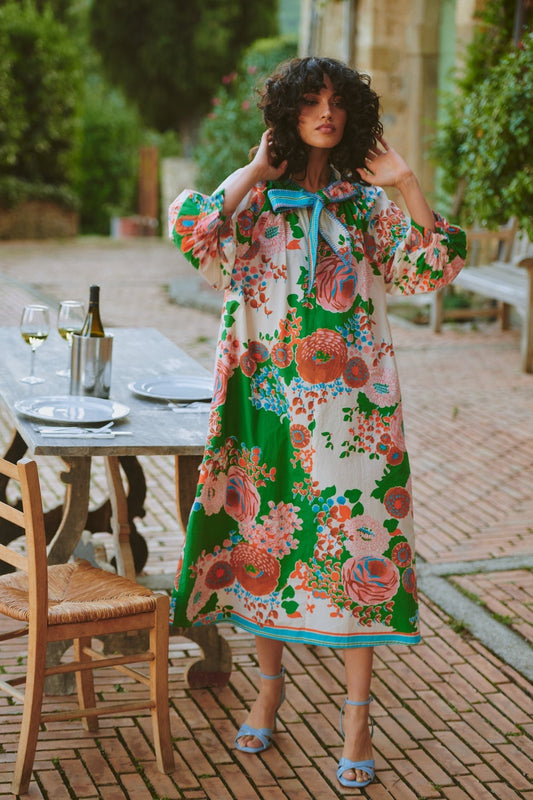 Woman in a floral dress standing outdoors near a dining table with wine glasses.