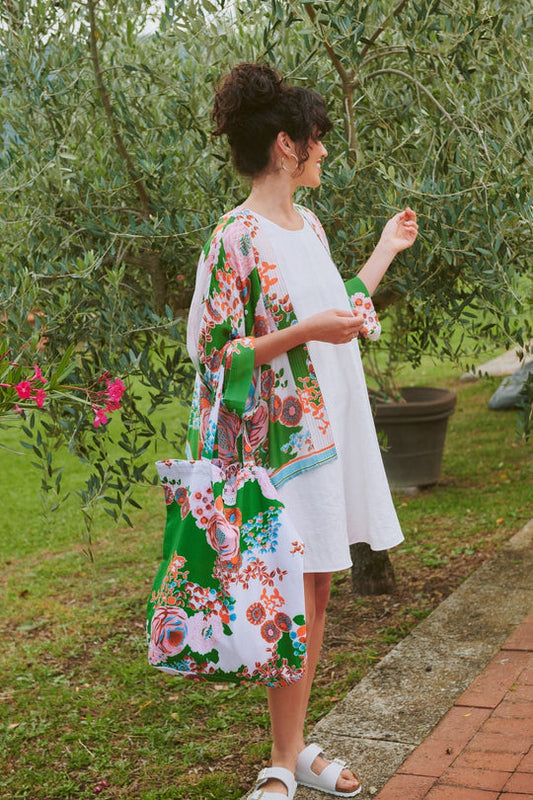 Woman in a floral kimono-style dress with matching tote bag standing outdoors near trees.