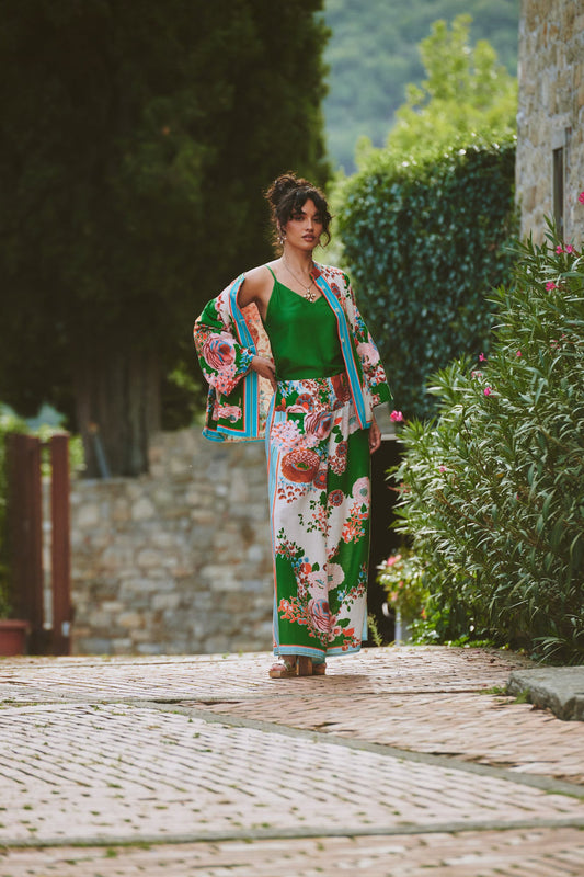 Woman in a floral kimono standing on a stone path with greenery and a stone building in the background