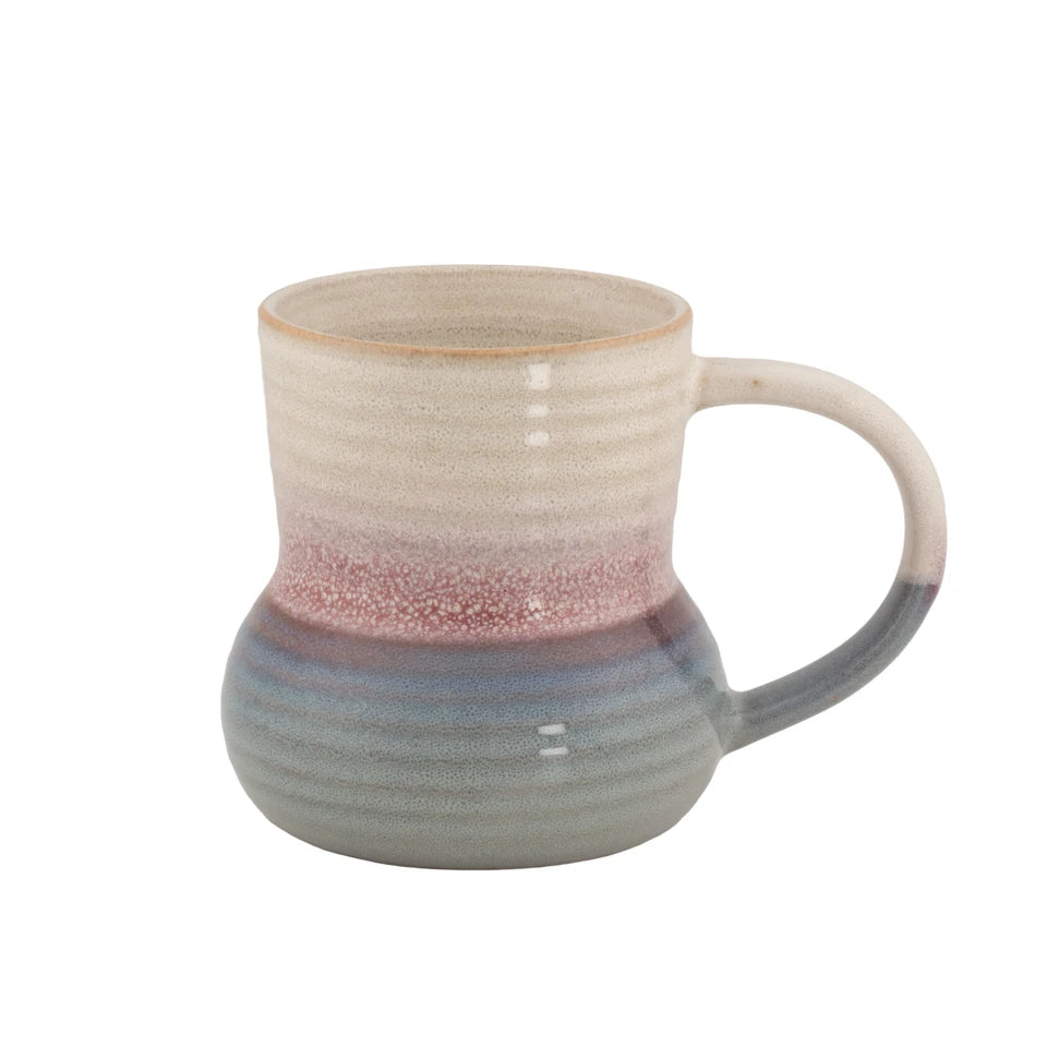 A handmade ceramic mug with a textured, ribbed finish, featuring a color gradient that transitions from a warm beige at the top, through a dusty rose band in the middle, to a muted blue-gray at the base and handle.