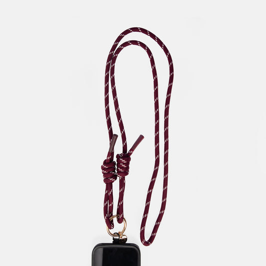 A burgundy and white patterned braided rope lanyard with a knotted loop and a gold metal ring, shown hanging from a black phone case against a light gray background.