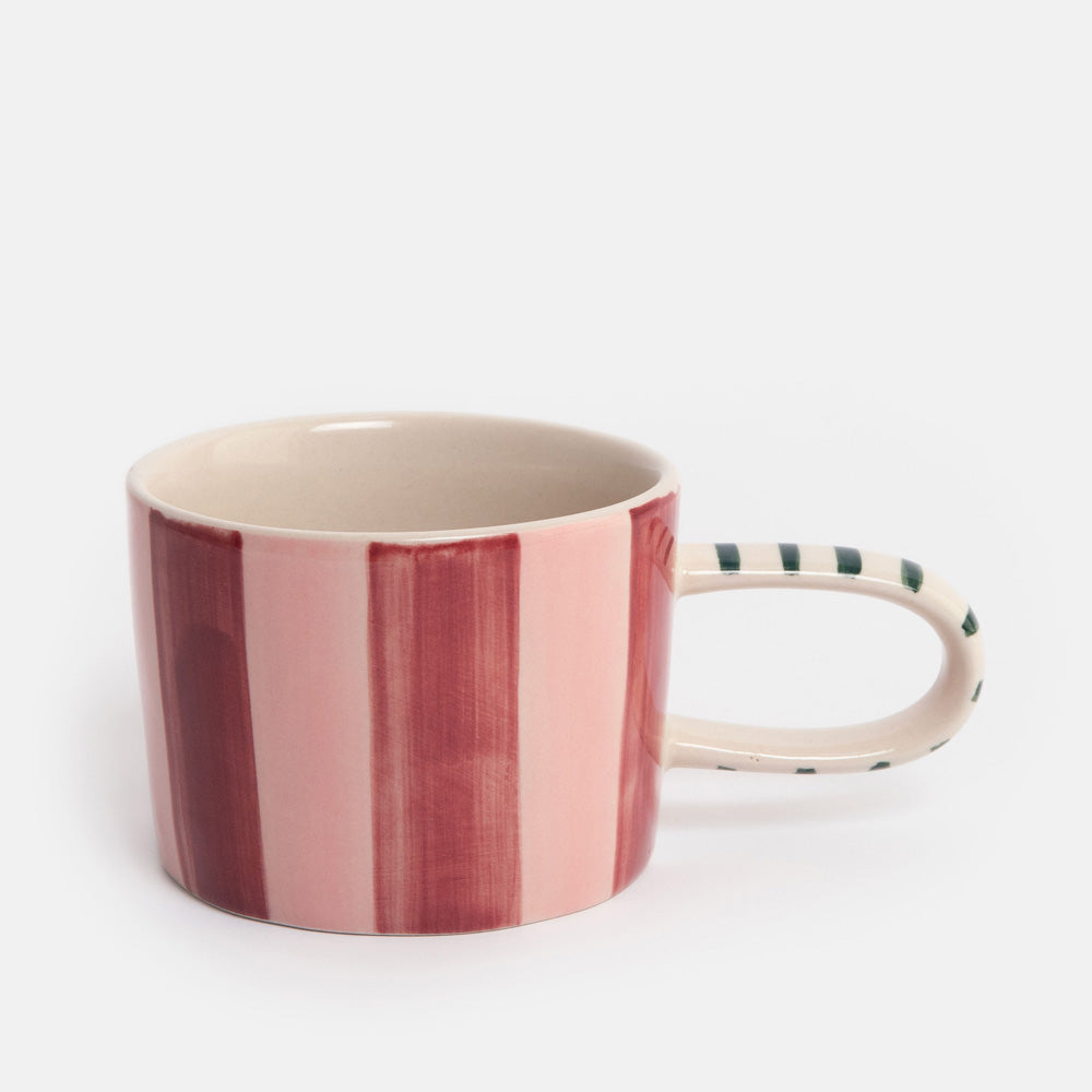 A ceramic mug with vertical pink and dark red stripes on the exterior, a cream-colored interior, and a handle decorated with dark green and cream stripes, set against a plain white background.