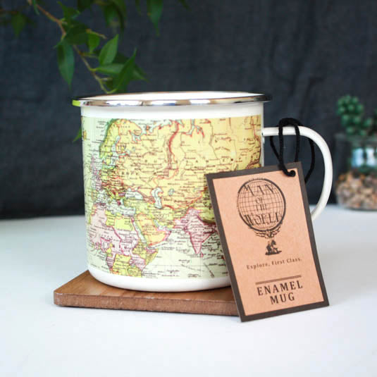 Enamel mug with world map design on a white surface with a tag, against a dark background.