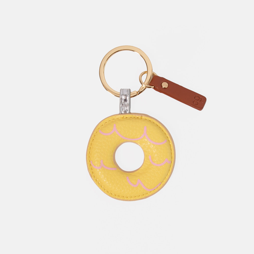 A yellow faux-leather donut keychain with pink icing details, a gold-tone split ring, and a brown leather tag on a light gray background.