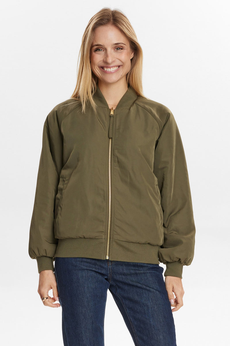 Numph Etera Reversible Jacket in Grape Leaf. Woman wearing an olive green bomber jacket and blue jeans on a white background