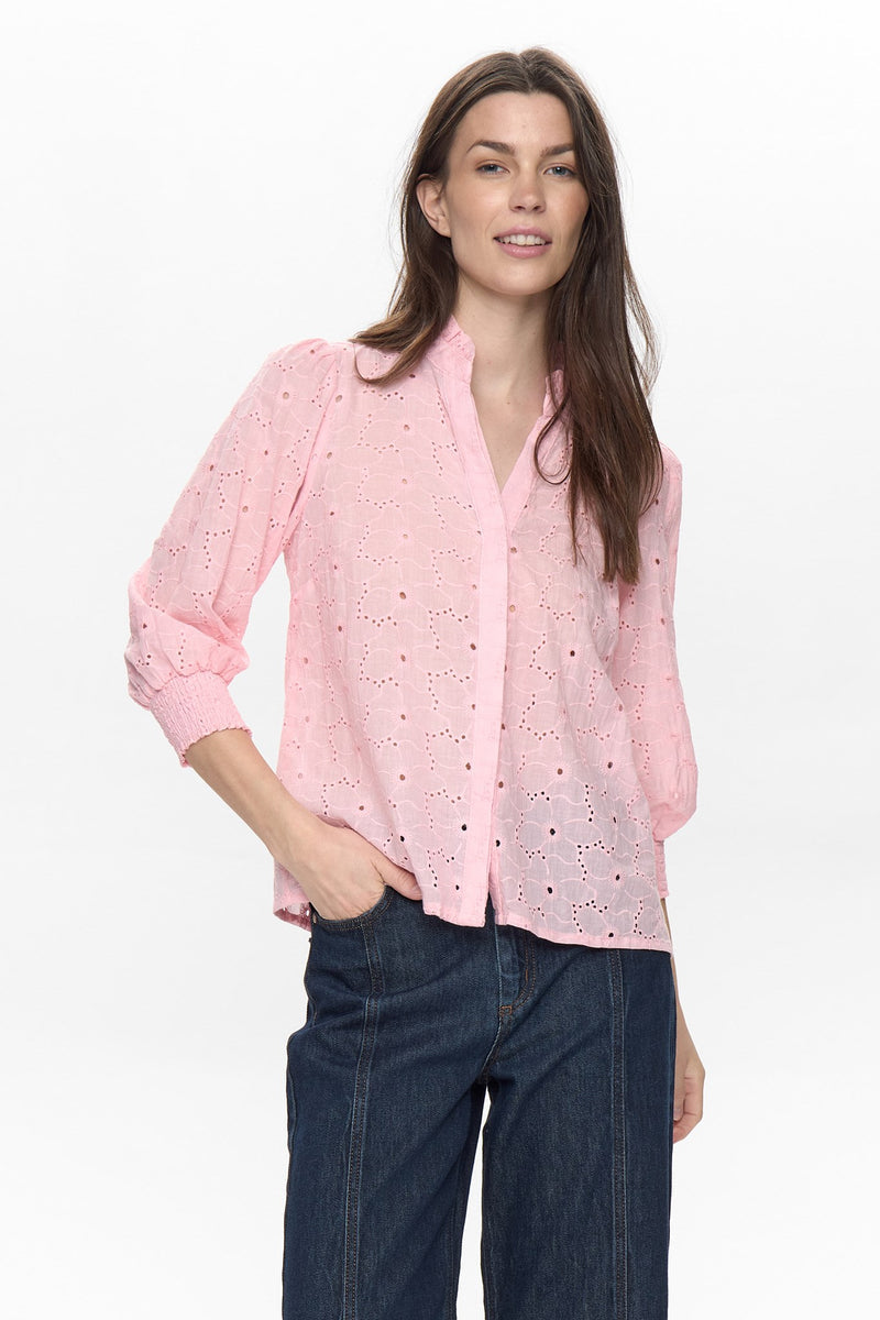 Woman wearing a pink blouse with lace details and blue jeans on a white background