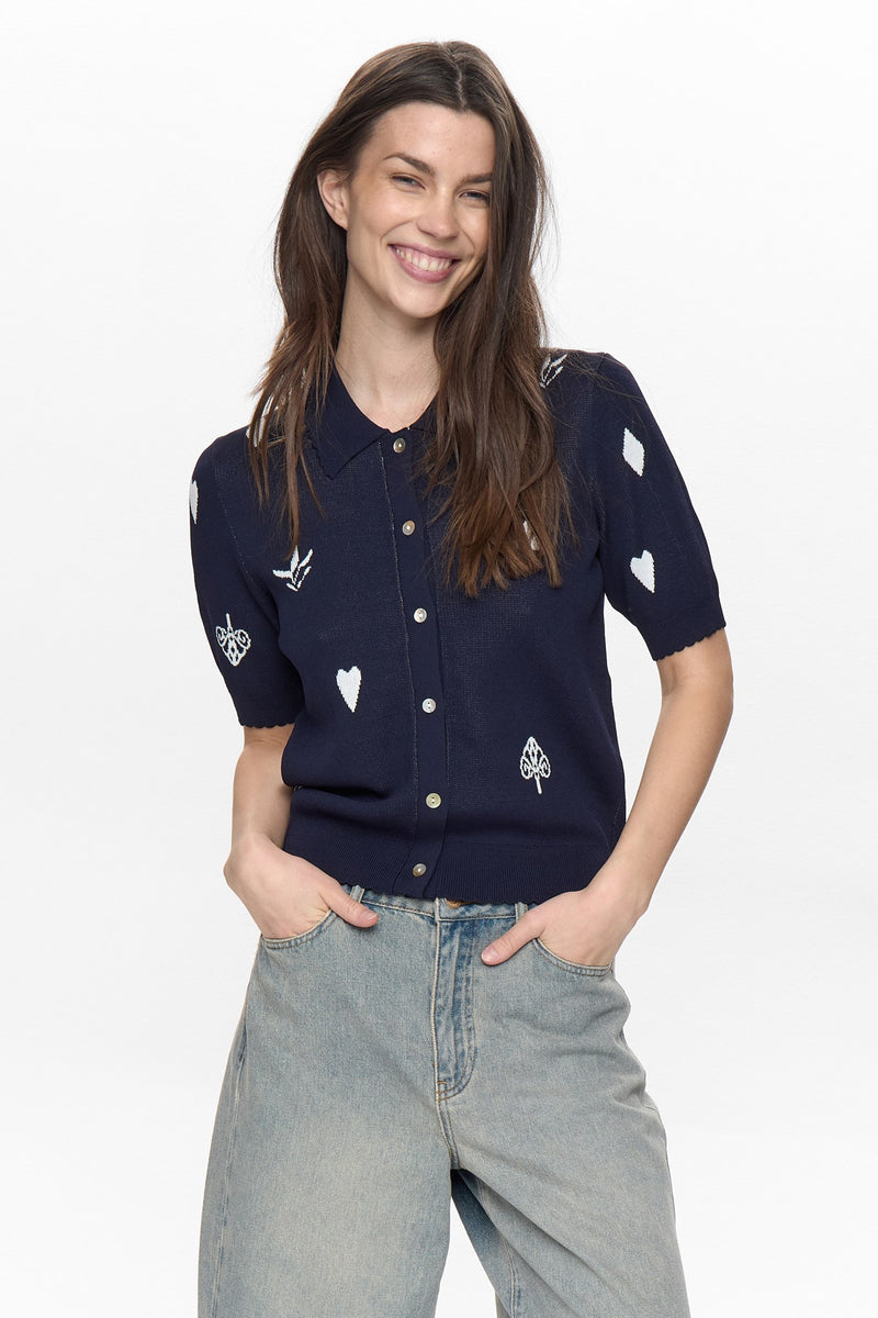 Woman wearing a navy blue shirt with white heart and leaf patterns on a plain background