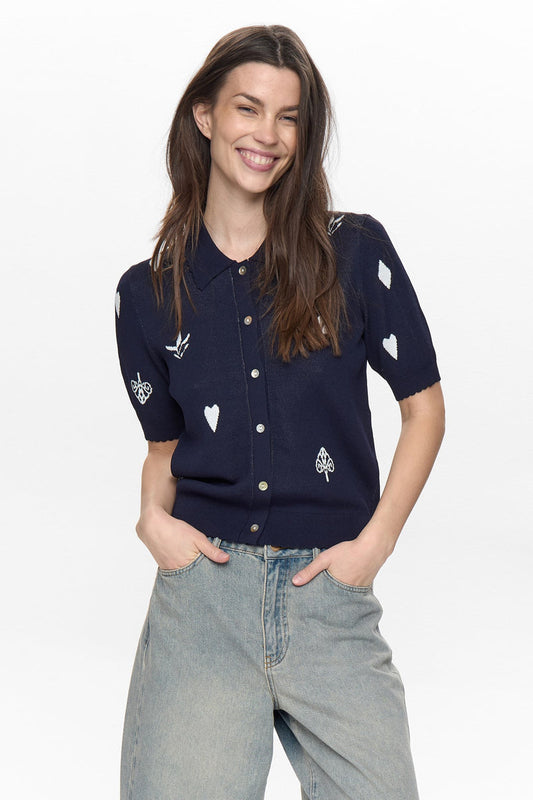 Woman wearing a navy blue shirt with white heart and leaf patterns on a plain background