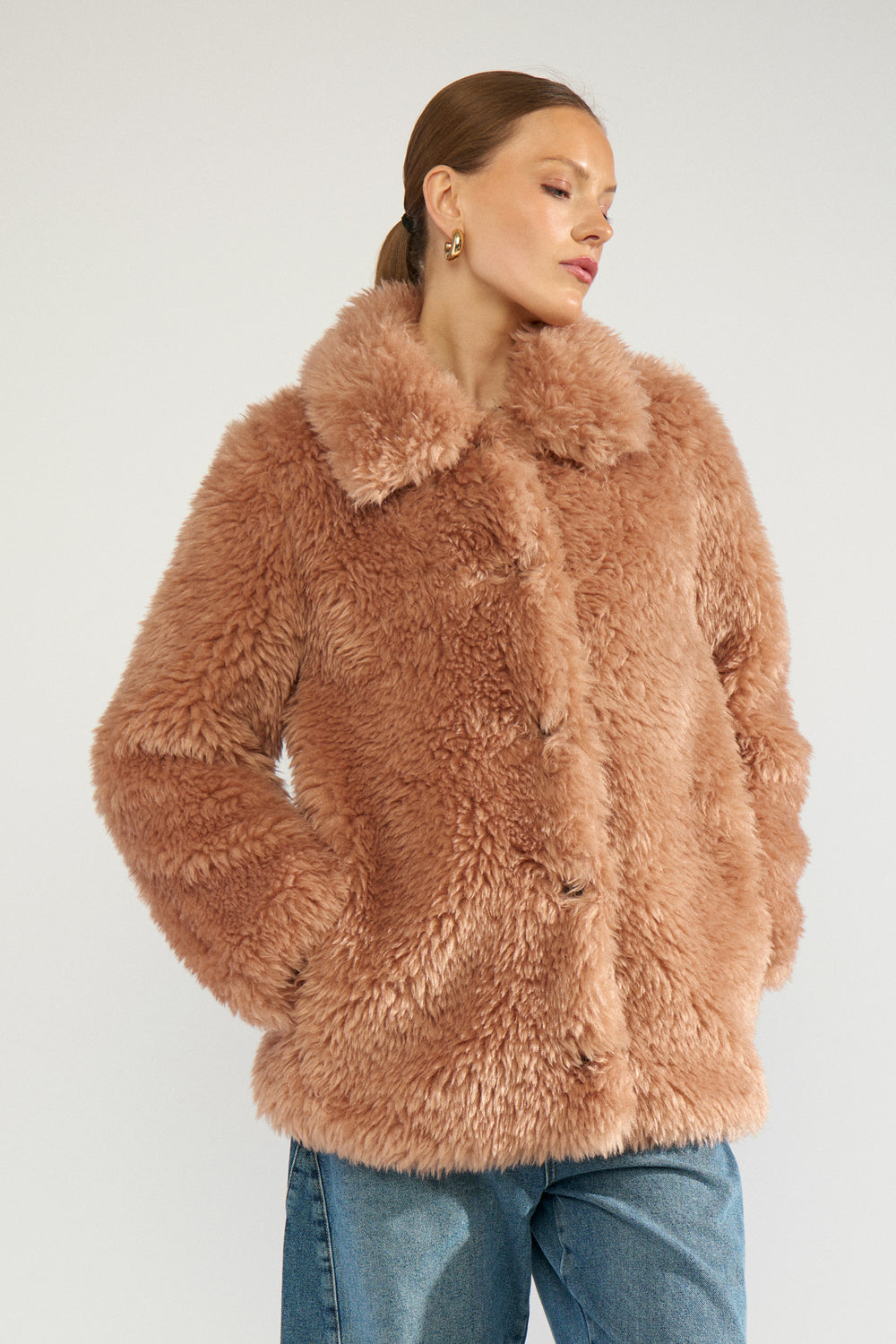 Numph Miska Jacket in Roebuck - the model wears a plush, shaggy faux-fur jacket in a dusty rose-brown colour, paired with blue jeans, photographed against a clean light grey studio background.