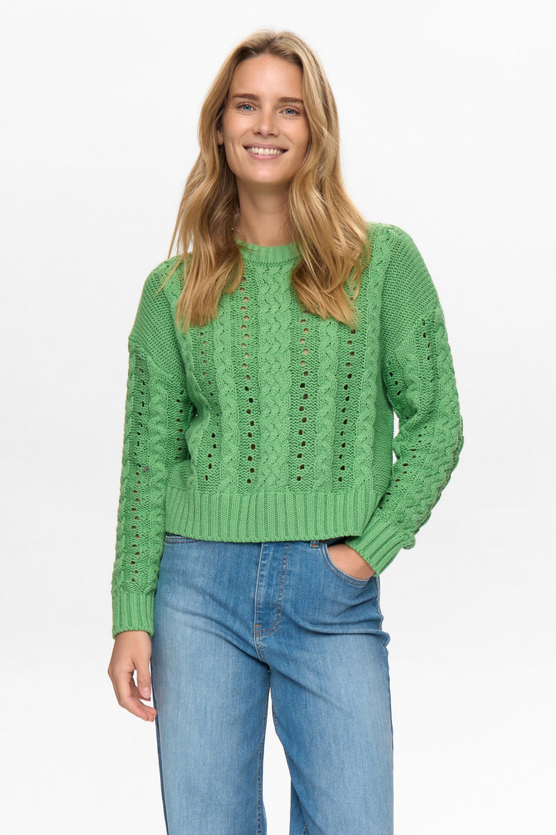 Woman wearing a green knitted sweater and blue jeans on a white background