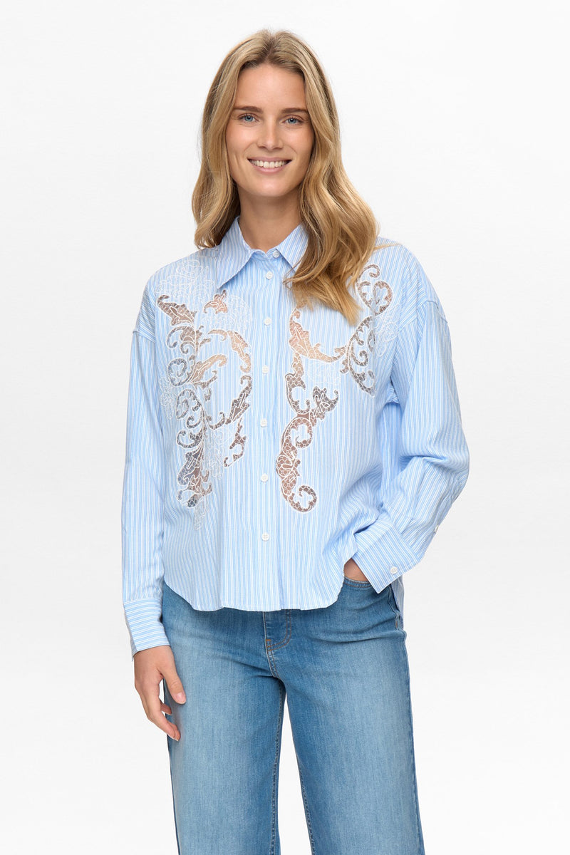 Woman wearing a light blue striped shirt with floral embroidery and jeans on a white background