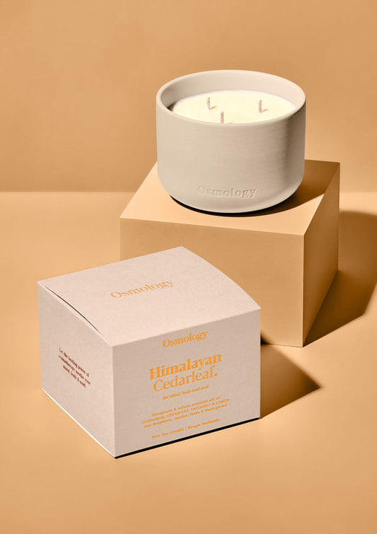 Candle with three wicks in a beige container with a matching box on a beige background