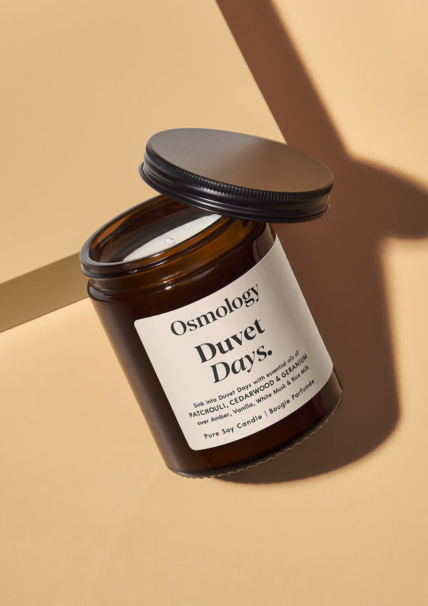 Osmology Duvet Days candle in a brown jar on a beige background