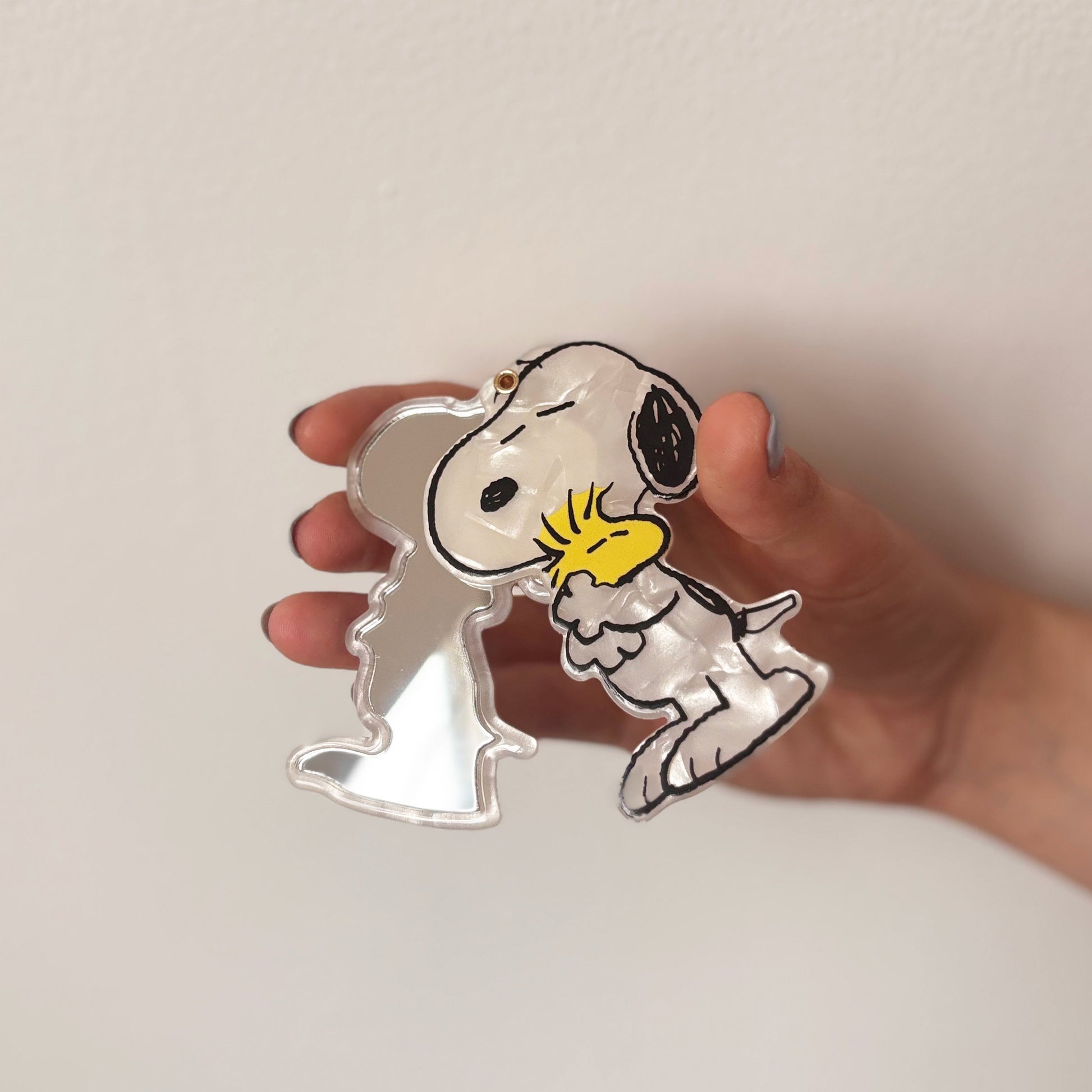 Metallic Snoopy keychain held by a hand on a light background