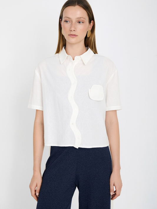 Woman wearing a white shirt with a pocket on a plain background