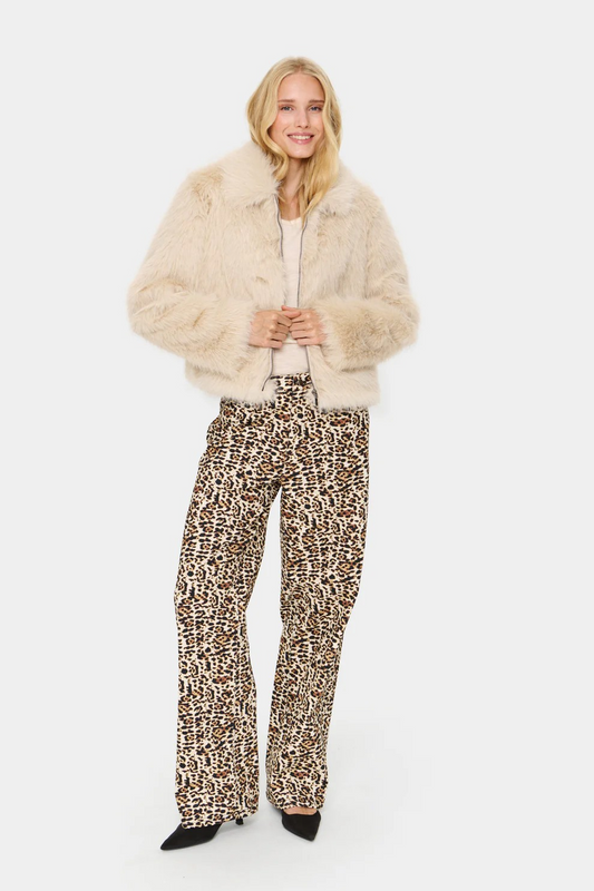 Woman wearing a cream fur jacket and leopard print pants on a white background