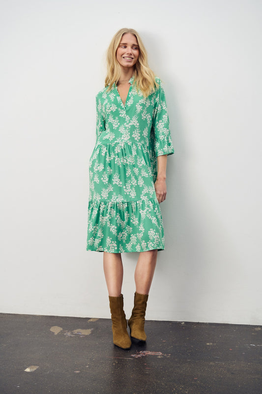 Saint Tropez Eda Dress in Greenbrair Flower Lane Woman wearing a green floral dress with brown boots against a white background