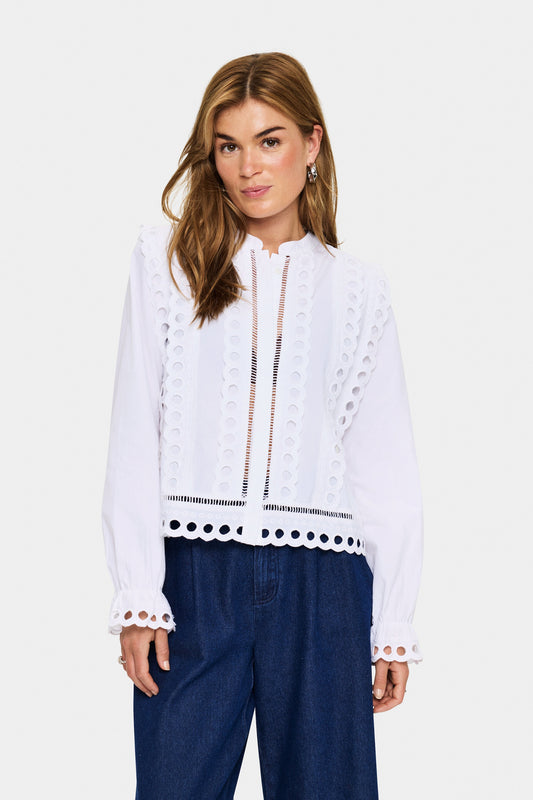 Saint Tropez Marlee Shirt in Bright White. Woman wearing a white blouse with lace details and blue pants on a white background