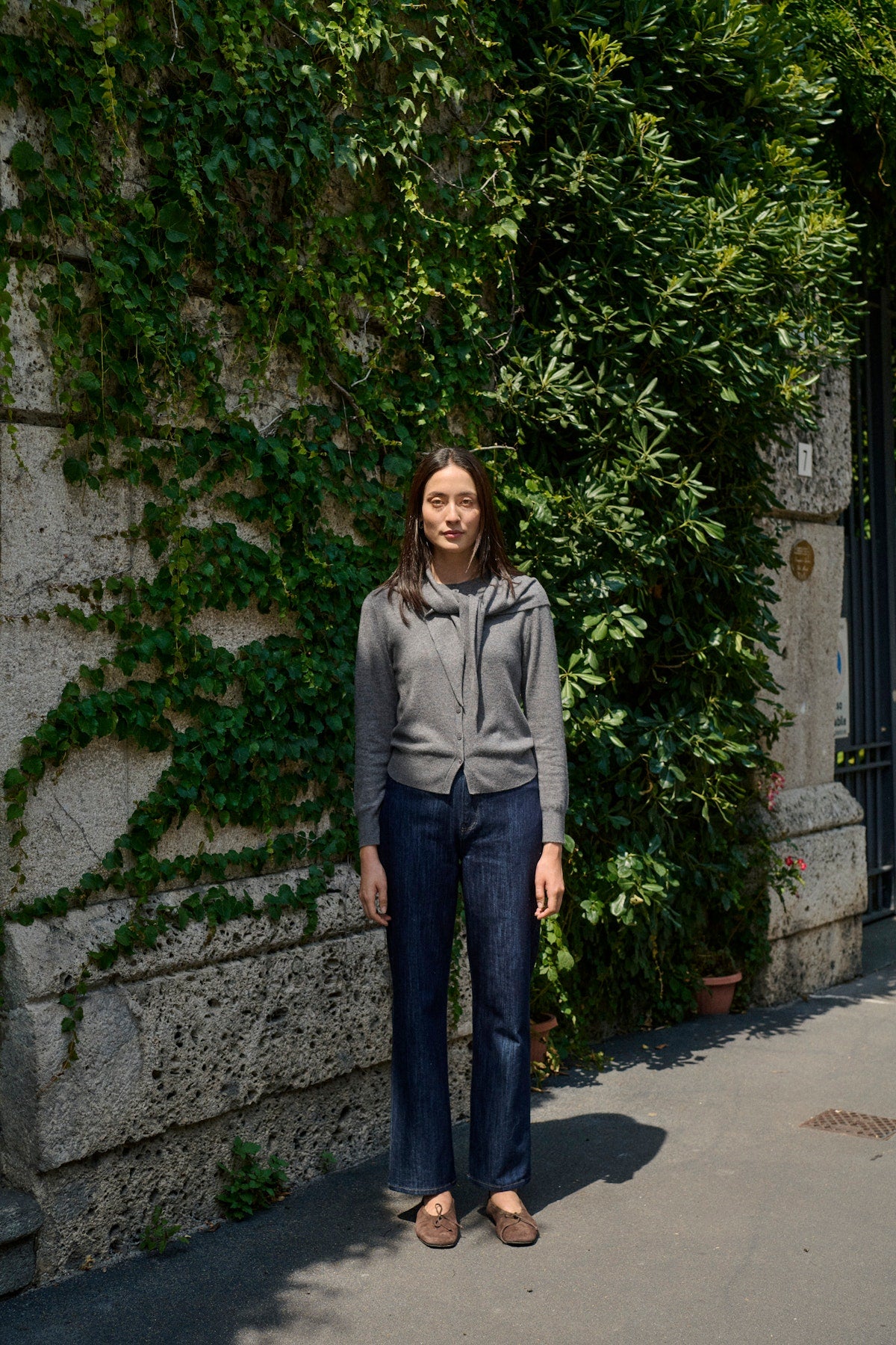 Soaked in Luxury Molina Scarf Cardigan in Grey Melange. Person standing in front of a wall covered in green ivy