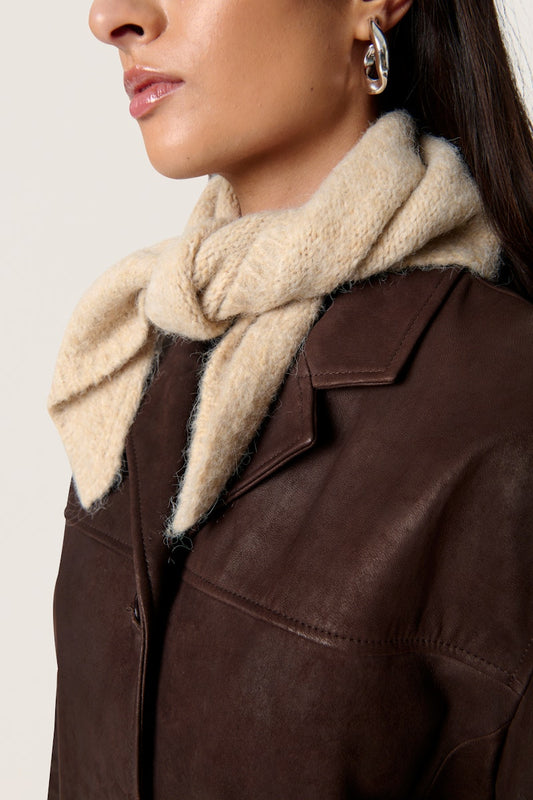Soaked in Luxury Pleoni Scarf in  Doeskin Melange. Close-up of a person wearing a brown leather jacket with a beige scarf around the neck on a white background