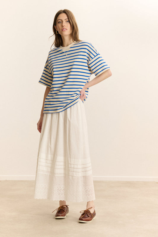 Woman wearing a blue and white striped shirt with a long white skirt on a plain background