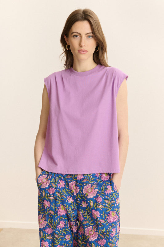 Woman wearing a purple sleeveless top and floral pants on a beige background