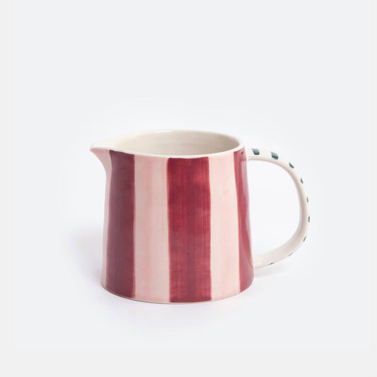 A ceramic pitcher with vertical stripes in deep red and light pink on the exterior, with a white handle and a dotted pattern on the side, set against a plain light gray background.