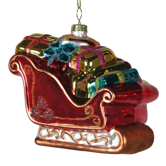 Decorative glass ornament of a red sleigh with gold and blue presents on a white background