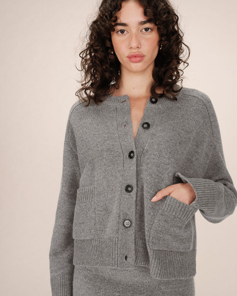 Woman wearing a gray cardigan with black buttons on a beige background
