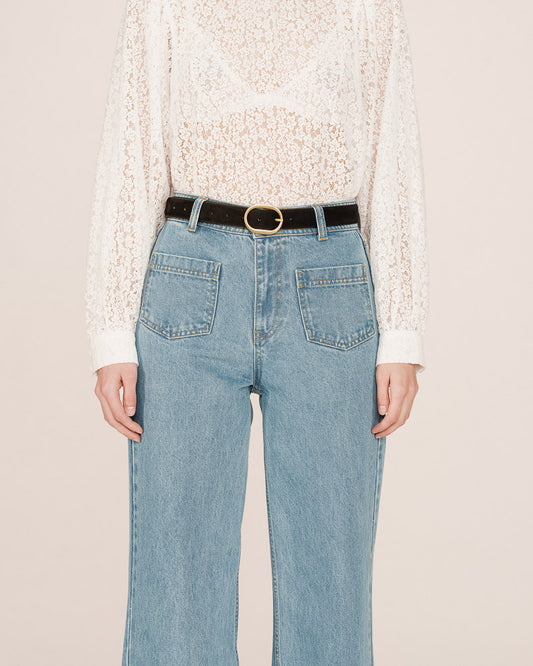 Person wearing light blue jeans with a white lace top on a beige background