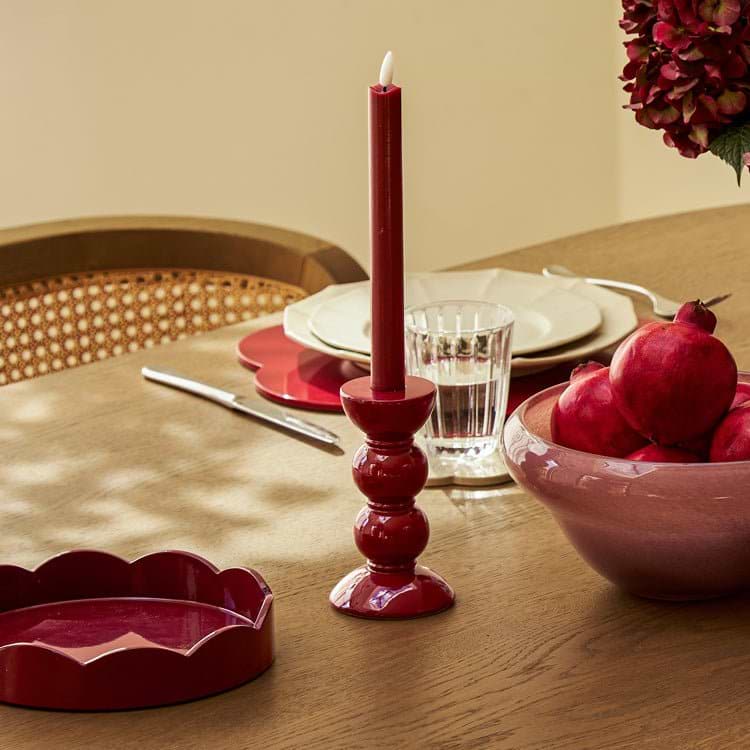 Cherry candlestick with a lit cherry candle on a wooden table with a bowl of pomegranates and a glass of water.