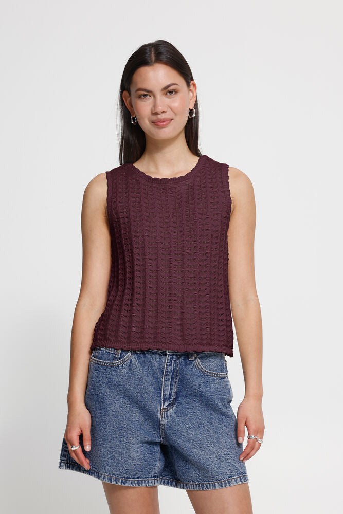 Woman wearing a maroon sleeveless top and denim shorts on a white background