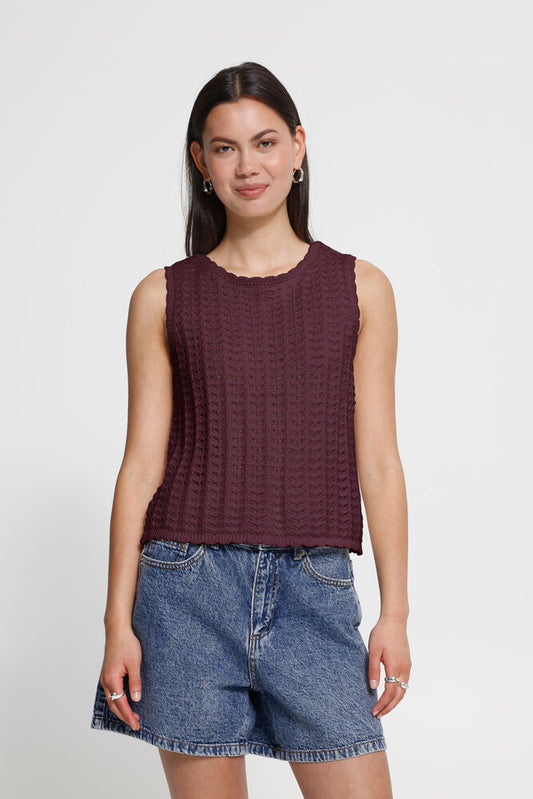 Woman wearing a maroon sleeveless top and denim shorts on a white background