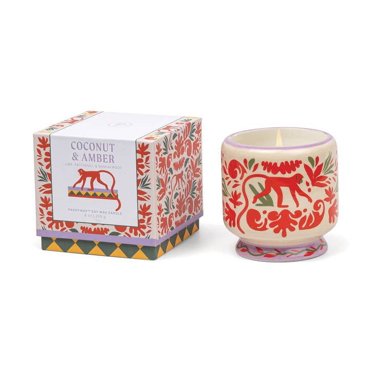 Decorative candle with floral and animal design next to its packaging on a white background