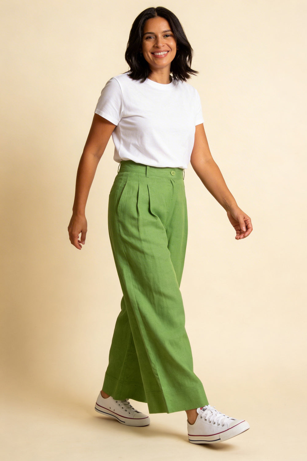Woman wearing a white t-shirt and green pants on a beige background