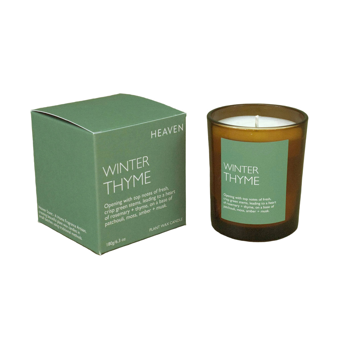 A winter thyme scented candle in an amber glass jar next to its sage green packaging box, labeled 'HEAVEN WINTER THYME', set against a solid sage green background.