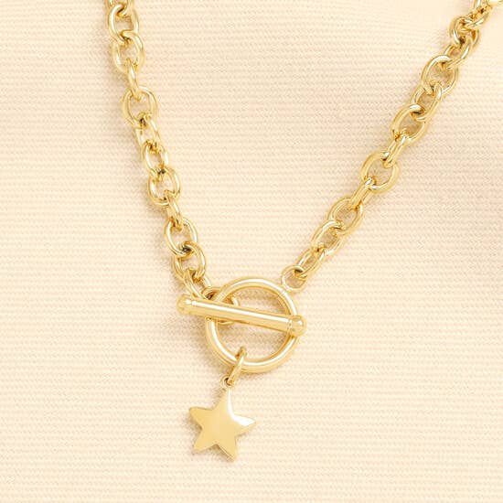 A gold chain necklace featuring a toggle clasp and a dangling star charm, displayed on a textured beige fabric background.