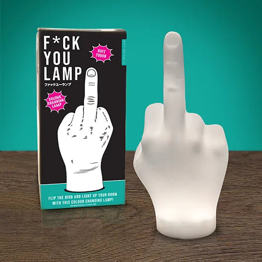 Lamp shaped like a hand giving the middle finger next to its packaging on a wooden surface with teal background.