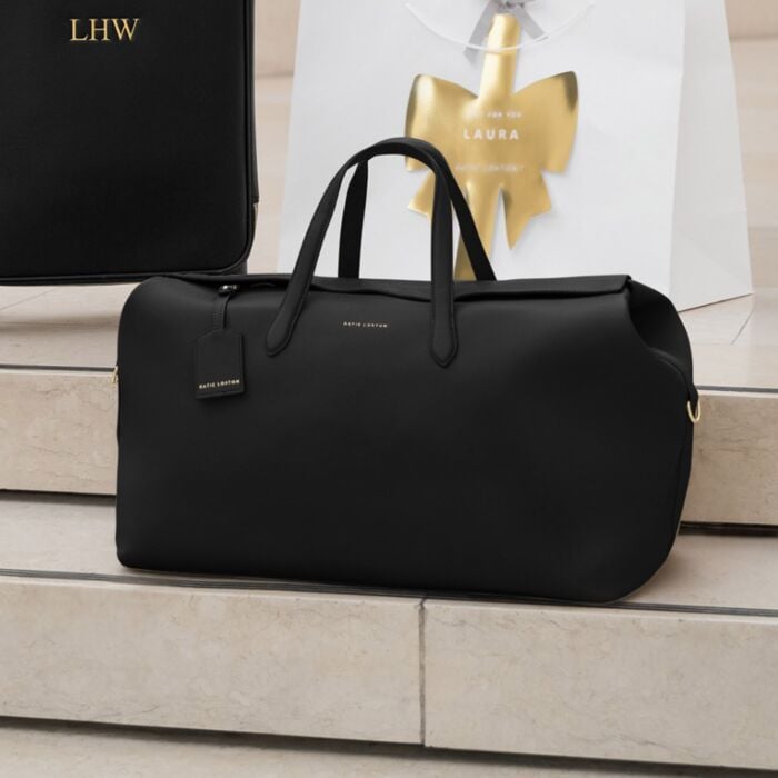 Black lether weekend bag with a visible brand tag on a light wooden surface.