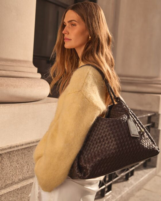 Woman holding a dark woven handbag in an urban setting