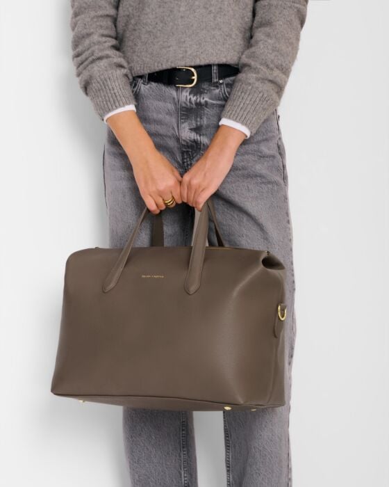 Person holding a brown handbag against a plain background