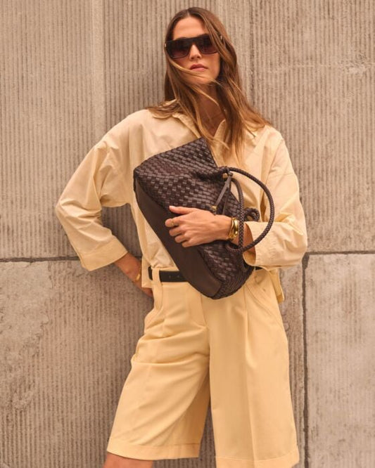 Woman holding a brown woven handbag against a textured wall.